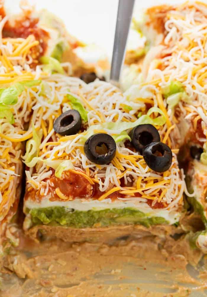 A spatula scooping up 7 layer dip from a casserole dish.