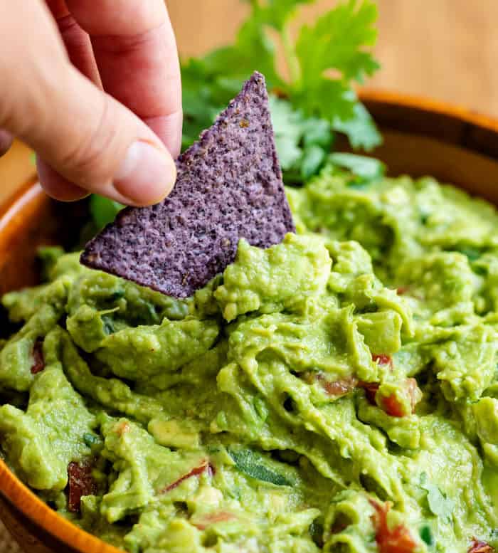 Close up view of a hand dipping a tortilla chip into a bowl of guacamole.