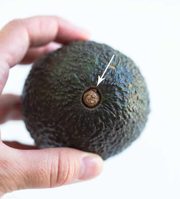 Close up shot of a hand holding an avocado with an arrow pointed at the pit.