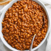 A white bowl filled with baked beans with a spoon.