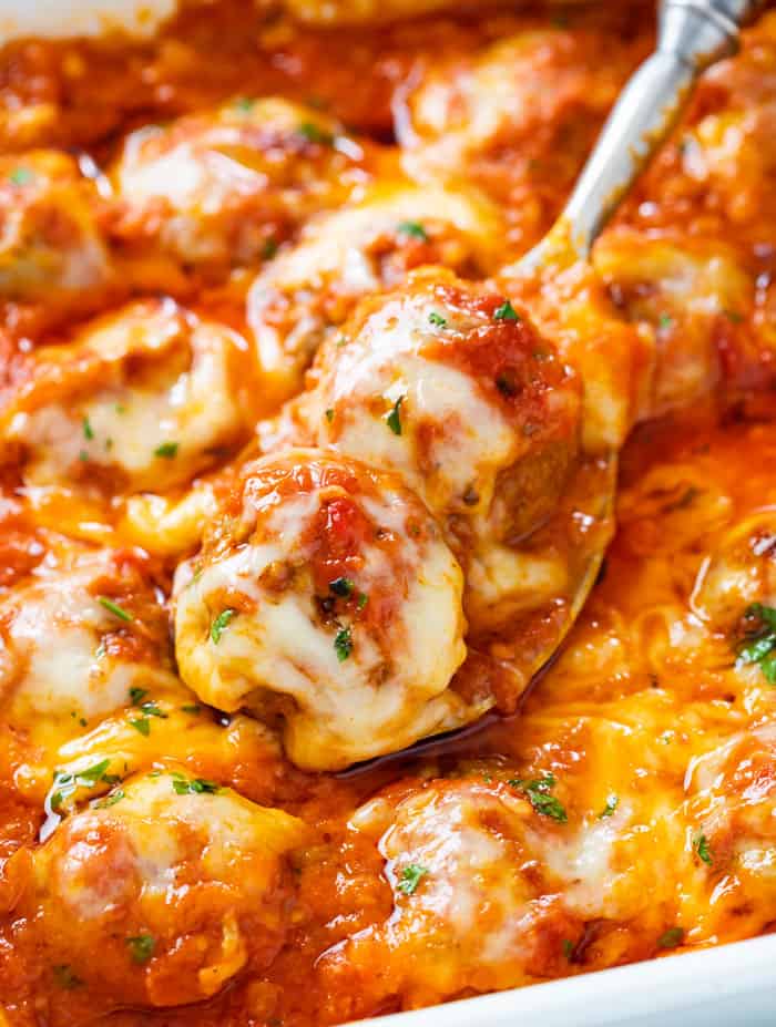 A spoon in a casserole dish full of baked meatballs in marinara sauce with melted cheese.