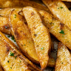 A pile of Baked Potato Wedges topped with parsley and seasoning.