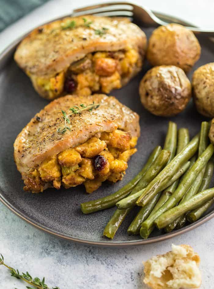 Golden brown pork chops filled with golden stuffing on a plate with green beans and roasted potatoes