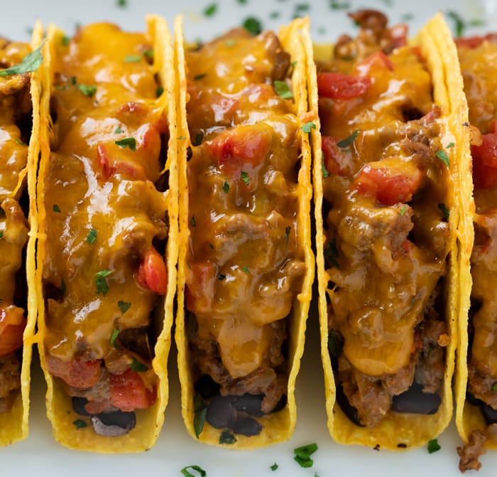 Baked Tacos filled with a creamy ground beef mixture with melted cheese lined up in a casserole dish.