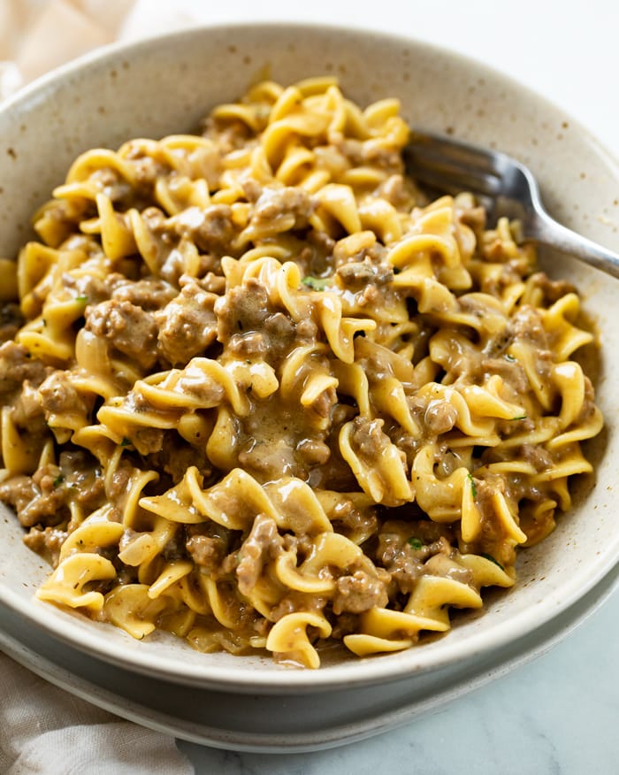 Beef and Noodles in a creamy gravy sauce on a white plate with a fork in the back.
