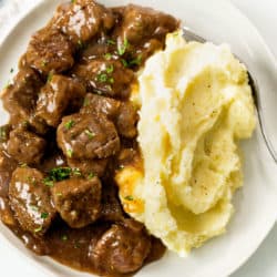 Tender Beef Tips and Gravy on a plate with Mashed Potatoes and fresh parsley.
