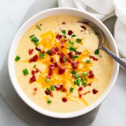 Beer Cheese Soup in a white bowl with bacon, cheese, and green onions on top.
