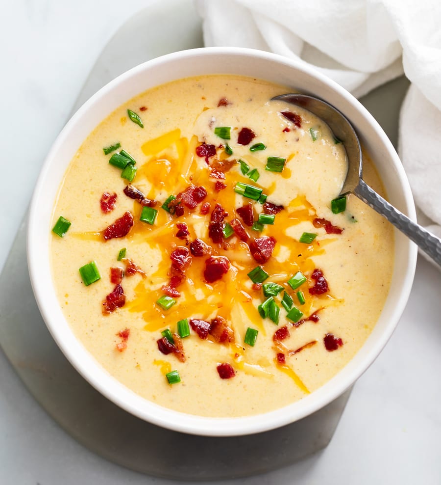 Beer Cheese Soup in a white bowl with bacon, cheese, and green onions on top.