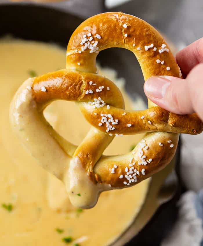 A hand holding a soft pretzel dipped in Beer Cheese Dip.