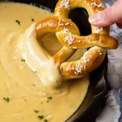 A cast iron skillet with beer cheese dip with a soft pretzel being dipped in it.