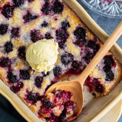 A casserole dish filled with Blackberry Cobbler with a scoop of ice cream on top.