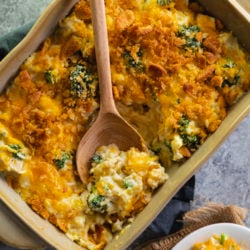 A casserole dish filled with chicken broccoli rice casserole with a wooden spoon in it.