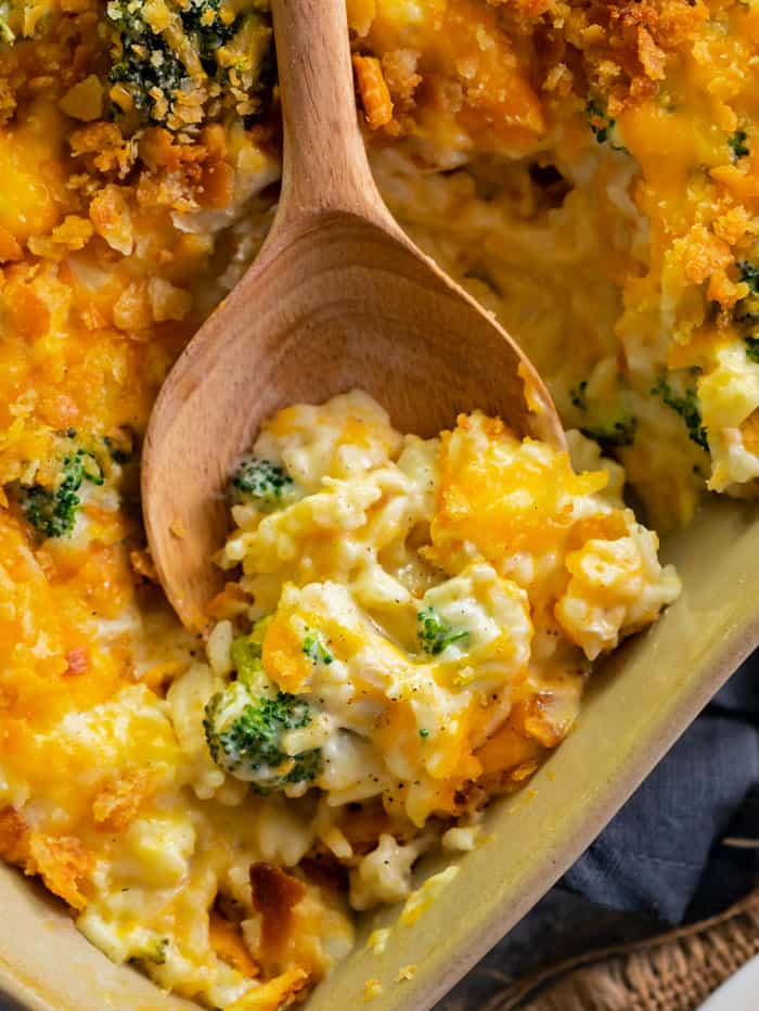 Casserole Dish filled with broccoli cheddar chicken and rice casserole with a wooden spoon scooping some out.
