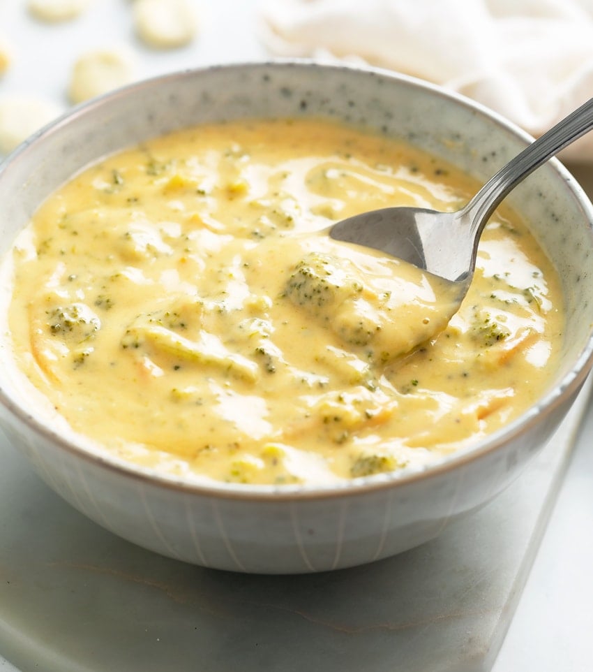 A bowl of creamy Broccoli Cheese Soup with a spoon scooping it up.