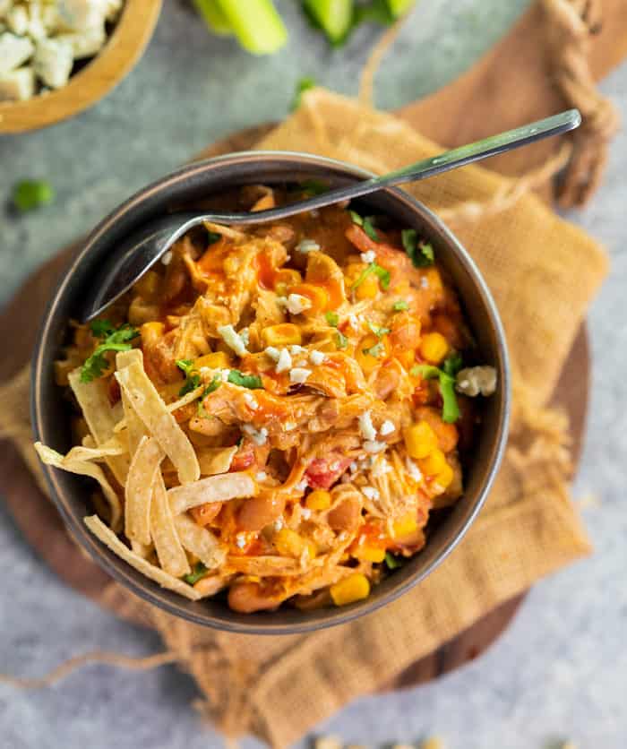 Overhead Shot of Buffalo Chicken Chili in a bowl with a spoon and crispy tortilla strips on top.