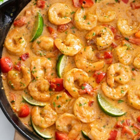 Cajun Shrimp in a skillet with sauce, bell peppers, and lime wedges.