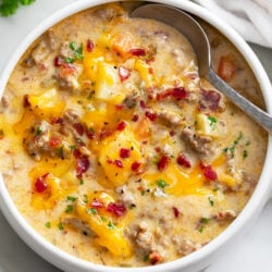 A bowl of Cheeseburger Soup with bacon on top and a spoon on the side.