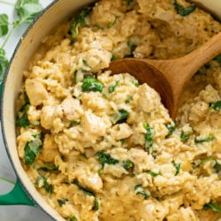 A dutch oven with Creamy Chicken and Rice with Spinach and a wooden spoon scooping it up.