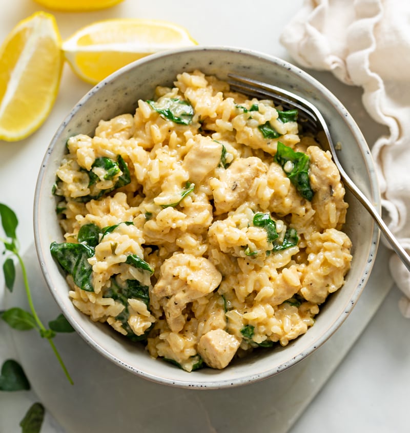 A bowl of Creamy Chicken and Rice with Spinach and lemons on the side.