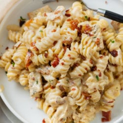 A white plate topped with creamy Chicken Bacon Ranch Pasta with crispy bacon on top.