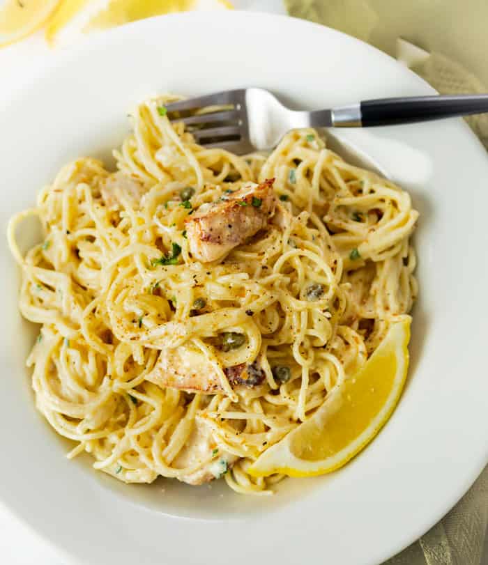 A white bowl filled with Chicken Caesar Pasta with chicken, capers, and lemons