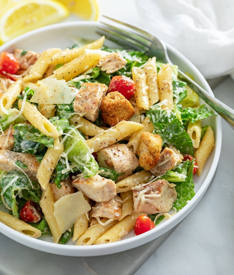 A white plate with Chicken Caesar Pasta Salad with a fork on the side.