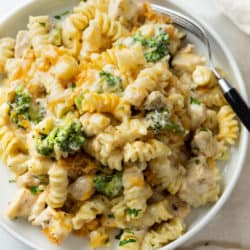 A white plate with Chicken Noodle Casserole with with a creamy mushroom cheese sauce and broccoli.