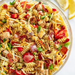 A glass bowl filled with Chicken Pasta Salad with bacon, tomatoes, cheese, and peppers.
