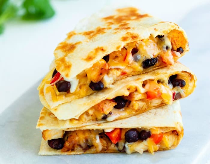 3 quesadillas stacked on top of each other on a white surface. Filled with black beans, chicken, and cheese.