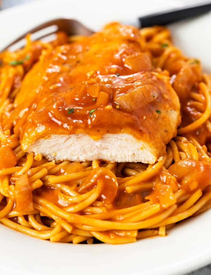 A slice of chicken breast on top of a plate of spaghetti in a red scallopini sauce.