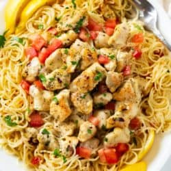 A white platter filled with Chicken Scampi with angel hair pasta and diced tomatoes with lemons and parsley.