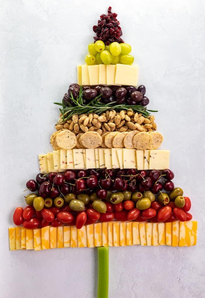 Overhead shot of cheese, crackers, almonds, olives, grapes, and tomatoes in the shape of a Christmas tree. 