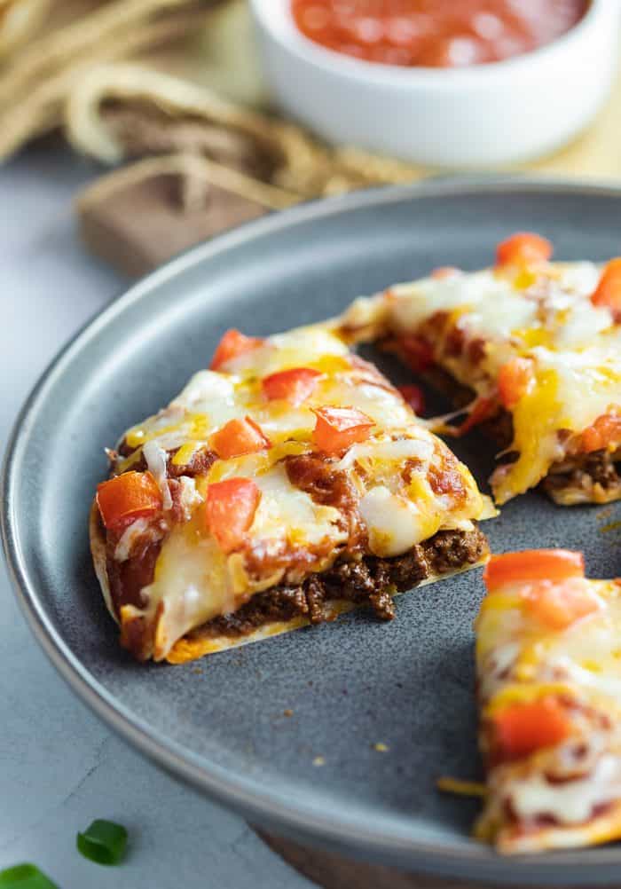 Slice of Taco Bell Mexican Pizza on a blue plate. Pizza is topped with melted cheese and tomatoes and filled with ground beef and refried beans. 