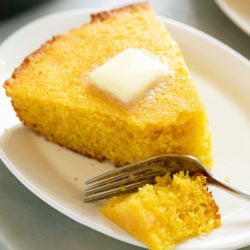 A white plate with a slice of Cornbread with butter on top and a fork.