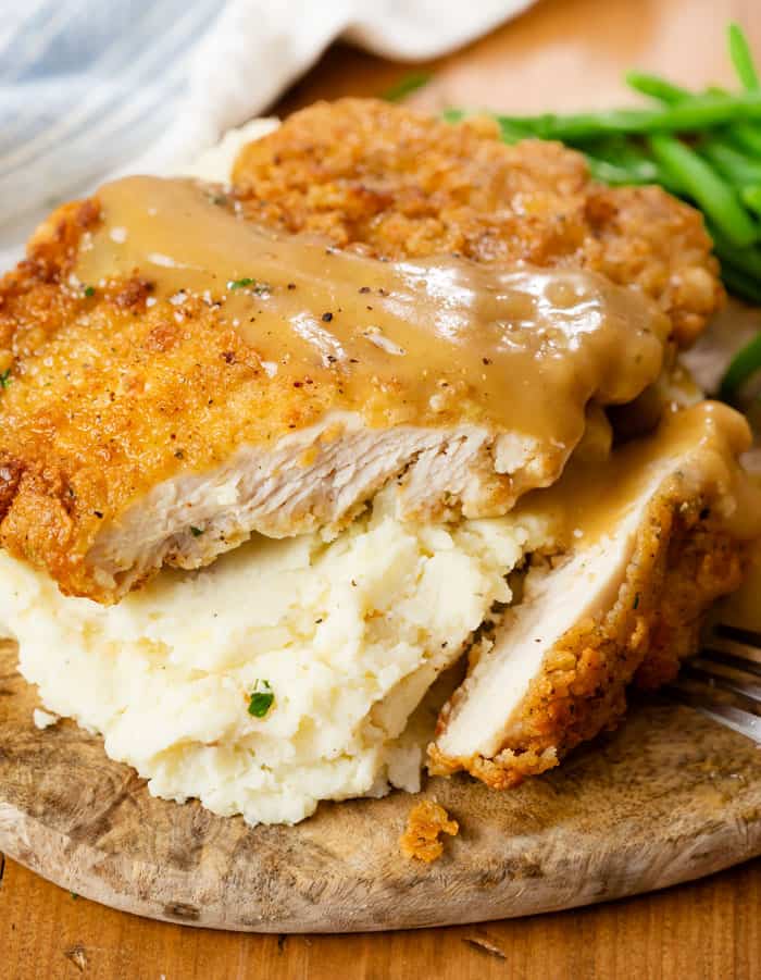 Country Fried Chicken over mashed potatoes with a slice cut into it and gravy on top.