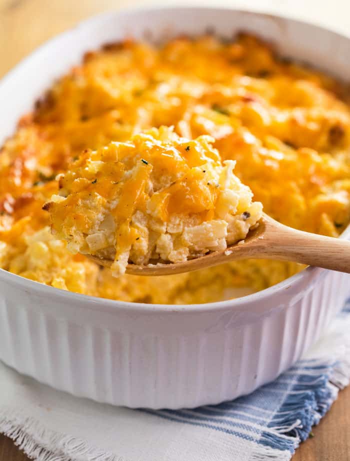 Wooden Spoon Scooping Cracker Barrel Hashbrown casserole out of a white casserole dish.