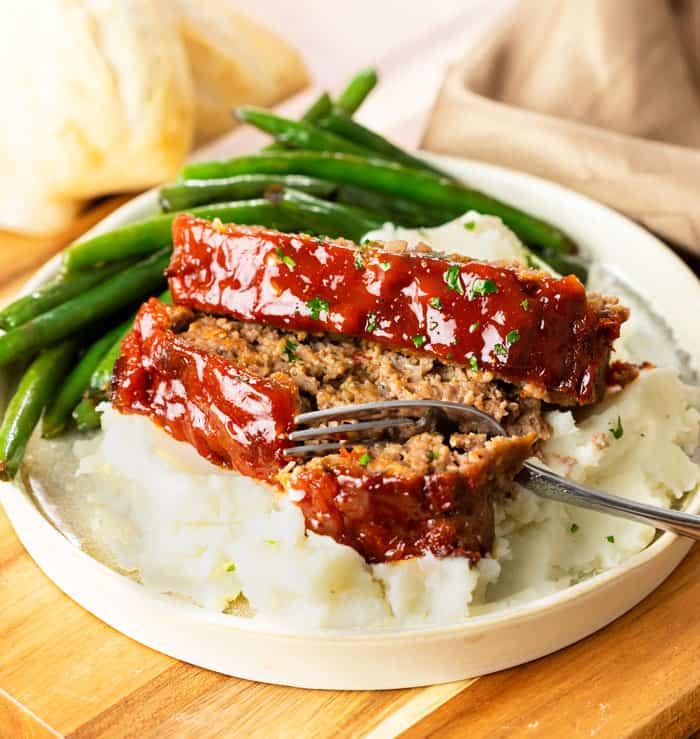 Two slices of Cracker Barrel meatloaf over mashed potatoes with green beans in the background.