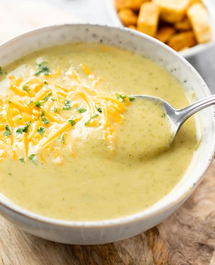A spoon scooping up cream of broccoli soup from a bowl.