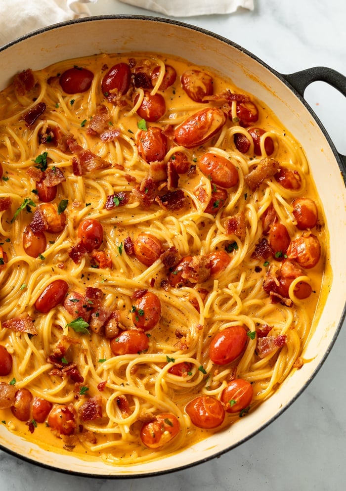 A skillet full of creamy bacon pasta with spaghetti, cherry tomatoes, and crispy bacon.