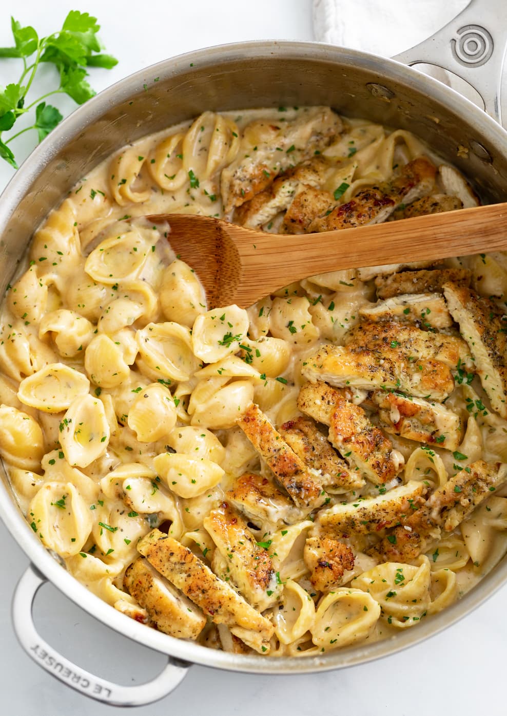 Creamy Chicken Pasta in a skillet with a wooden spoon and chopped parsley. 