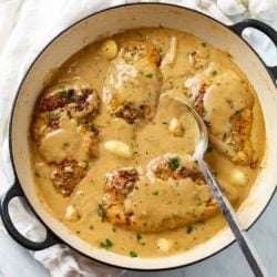 A skillet filled with Creamy Garlic Chicken in a sauce with whole garlic cloves.