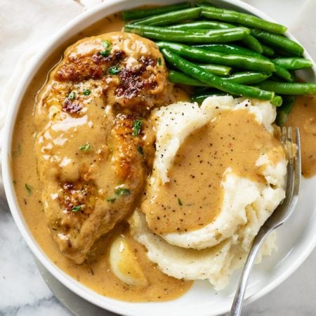 A white plate with Creamy Garlic Chicken, Mashed Potatoes, Green Beans, and Gravy.