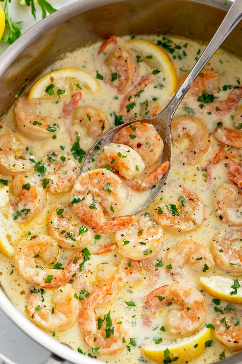 A skillet filled with shrimp in a creamy garlic sauce with fresh lemons and parsley.