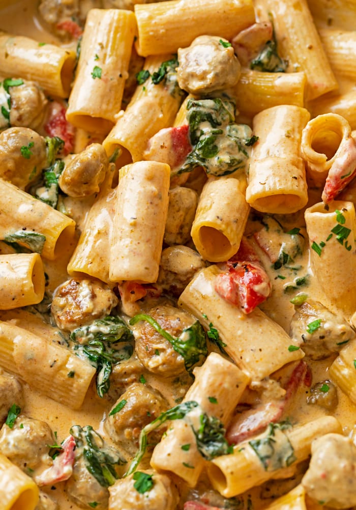 A close up view of rigatoni noodles in a Creamy Sausage Pasta with red peppers and spinach.