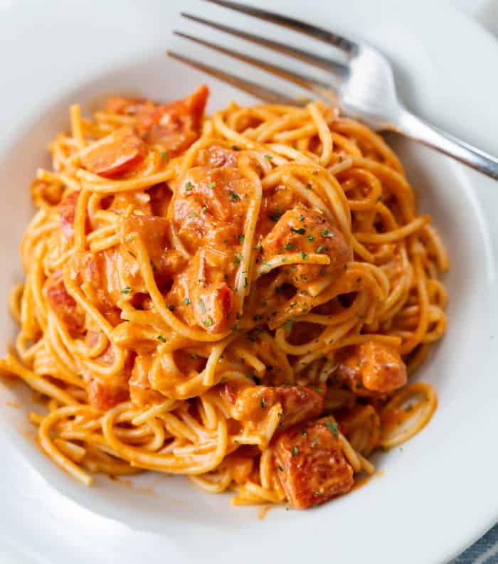 A white plate filled with creamy tomato pasta with a fork on the side.