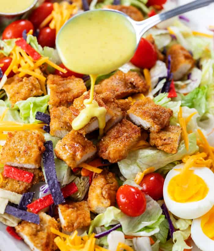 A spoon drizzling honey mustard over a crispy chicken salad.