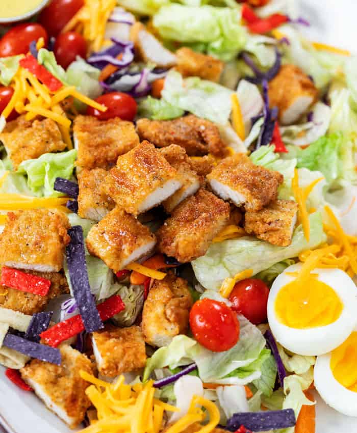 Crispy Chicken Salad with breaded chicken strips, lettuce, tomatoes, hard boiled eggs, cheese, and crispy tortilla crisps.