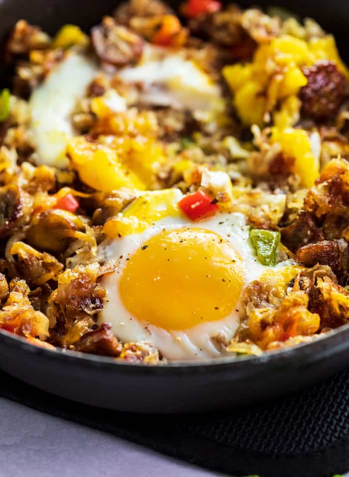 A close up shot of a baked egg in an iron skillet with hash, sausage, and bell peppers