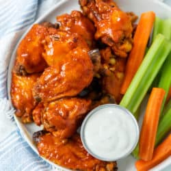 A plate with Buffalo Chicken Wings with a cup of blue cheese with celery and carrot sticks.