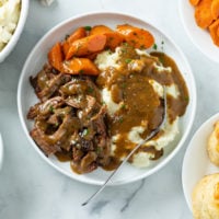 Mississippi Pot Roast on a white plate with potatoes, gravy, and carrots.